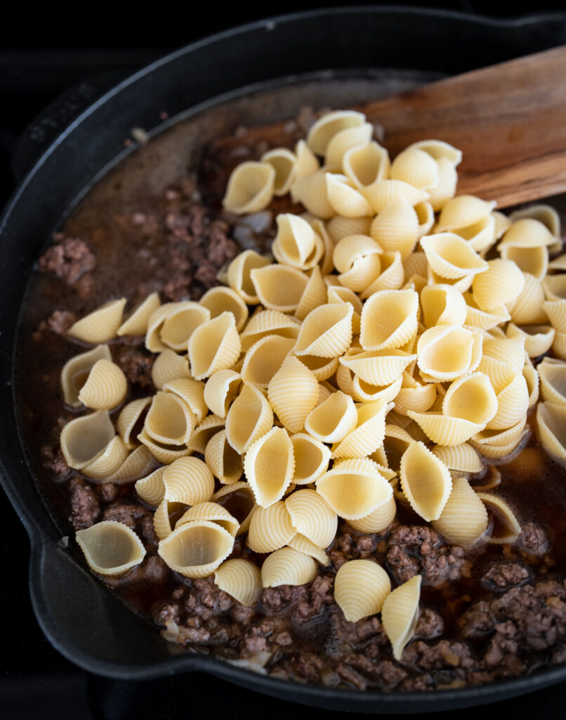 pasta shells on top of ground beef and beef broth in a skillet