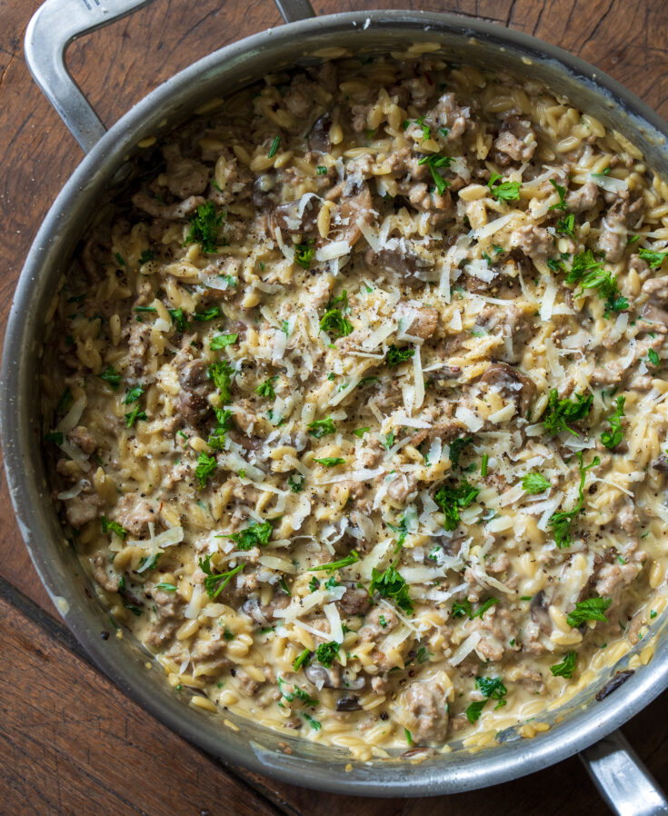 sauté pan with ground turkey and mushroom orzo garnished with parsley and grated cheese