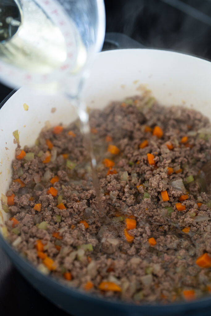 adding white wine to the cooked ground beef and veggies