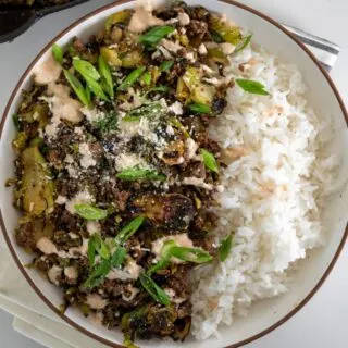 ground beef and brussels sprouts in a bowl with rice, spicy crema, scallions, and cotija cheese