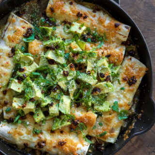 ground turkey enchiladas cooked in a cast iron skillet and garnished with diced avocado and cilantro