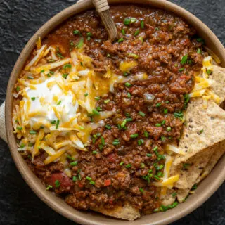 bowl of bison chili with tortilla chips, shredded cheese, Greek yogurt, and chives